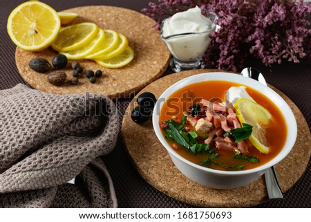 Soup Solyanka is a combined meat soup with smoked meat , various types of meat and tomato paste, serving dishes with sour cream, lemon and fresh herbs. Black olives on the table and a sprig of fresh f Stock fotó © 