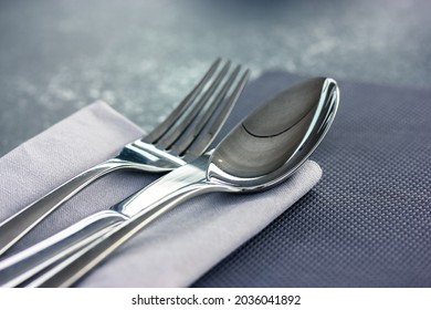 The soup spoon and metal fork lie on a gray napkin on a black grey surface top view. Table setting, cloth in a restaurant, cafe, at home kitchen. Gray textile towel. Flatware close up view from above.