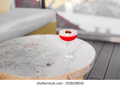 Sour pink cocktail with a flower on a marble table on a terrace bar 