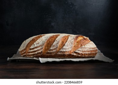 Sourdough bread. Freshly baked organic wheat bread on dark background,  with linen tablecloth. Side view.