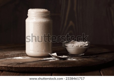 Sourdough bread starter with bubbles with white flour on dark wooden rustic background, fermentation, natural homemade baking and cuisine concept