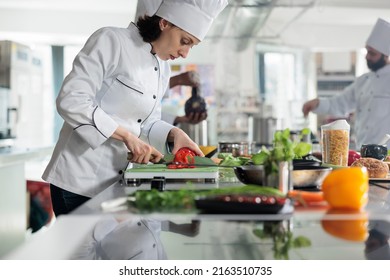 Sous chef chopping red pepper vegetable for gourmet dish served at dinner in restaurant. Head cook in professional kitchen cooking organic food while cutting fresh vegetables. - Powered by Shutterstock