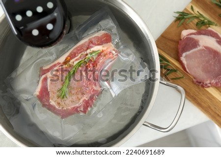 Sous vide cooker and vacuum packed meat in pot on white table, top view. Thermal immersion circulator