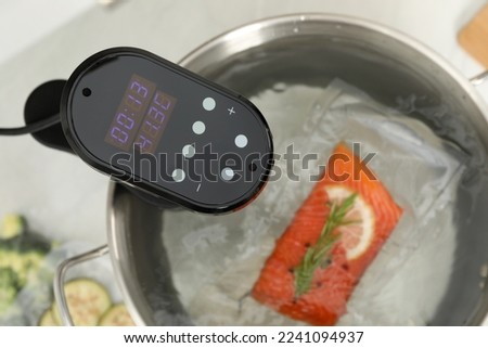 Sous vide cooker and vacuum packed salmon in pot on white table, closeup. Thermal immersion circulator