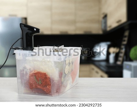 Sous vide cooker and vacuum packed food products in box on wooden table in kitchen, space for text. Thermal immersion circulator