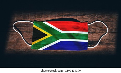 South Africa National Flag At Medical, Surgical, Protection Mask On Black Wooden Background. Coronavirus Covid–19, Prevent Infection, Illness Or Flu. State Of Emergency, Lockdown