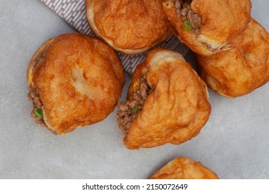 South African vetkoek, deep fried savory dough filled with saucy savory mince on mottled grey background with copy space

