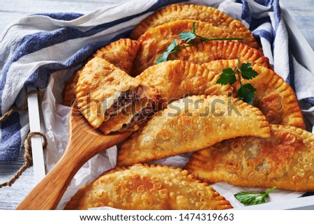 South american food: crispy fried empanadas with ground beef stuffing served on a white serving tray on white wood background with a kitchen dish towel, close-up