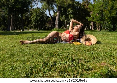 South American girl in a bikini lying on the grass. With a book, with a hat and 4 oranges. Summer relax concept