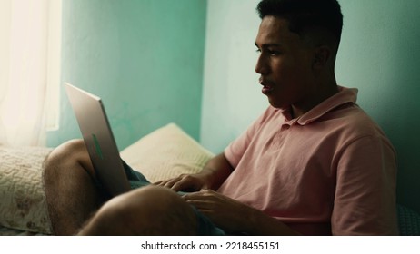 South American Hispanic Young Man Using Laptop In Bedroom. A Brazilian Latin Person Browsing Internet Online Sitting In Bed At Home Looking At Computer Screen 3