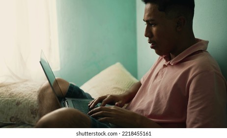 South American Hispanic Young Man Using Laptop In Bedroom. A Brazilian Latin Person Browsing Internet Online Sitting In Bed At Home Looking At Computer Screen 3