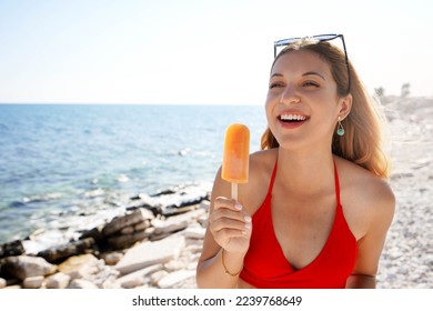 South American laughing girl eating orange ice lolly on the beach on summer - Powered by Shutterstock