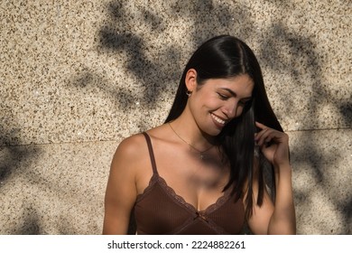 South American Woman, Young And Beautiful, Brunette, Wearing A Brown Dress, Posing Leaning Against A Wall With A Sensual And Provocative Attitude. Concept Beauty, Sensuality, Provocation, Flirting.