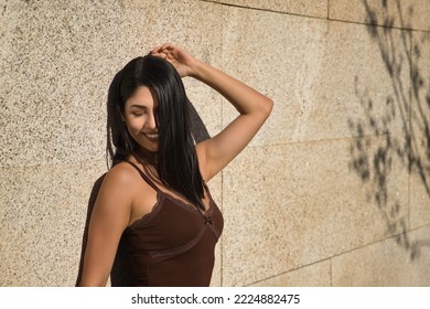 South American Woman, Young And Beautiful, Brunette, Wearing A Brown Dress, Posing Leaning Against A Wall With A Sensual And Provocative Attitude. Concept Beauty, Sensuality, Provocation, Flirting.