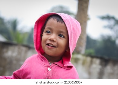 A South Asian Child In A Pink Coat Posing For A Photo Outdoors