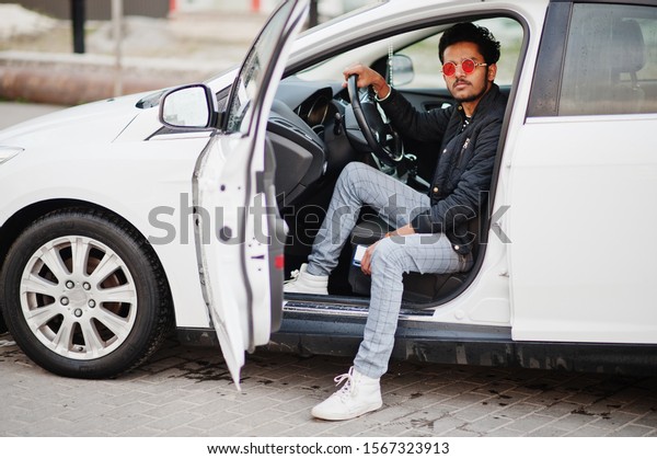 South asian man or indian male
wear red eyeglasses sitting inside his white transportation
car.