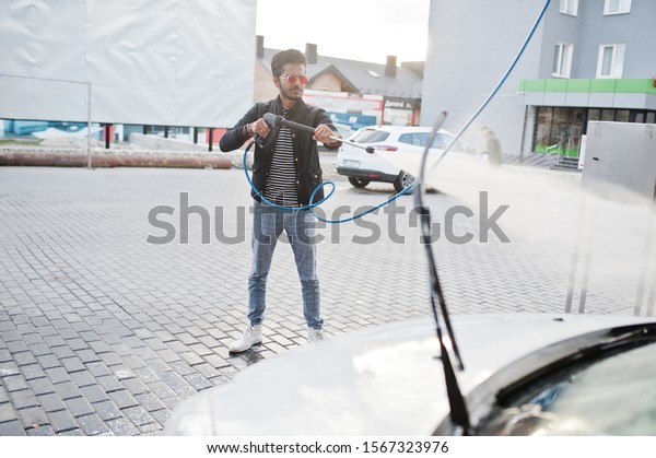 South asian man or indian male washing his white\
transportation on car\
wash.