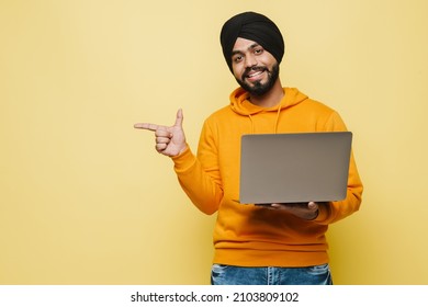 South Asian Man Pointing Finger Aside Laptop While Using Laptop Isolated Over Yellow Wall