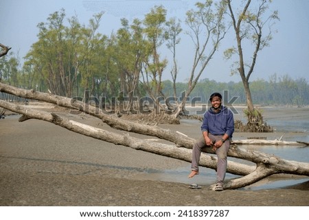 South asian young boy sitting on a fallen stem of a tree in front of a mangrove forest 