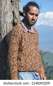 A south asian young man looking down while leaning against tree in the nature 