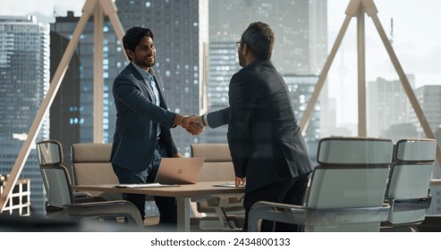 South Asians Business Partners Striking a Successful Deal at a Corporate Modern Meeting Room. Two Young Indian Businessmen Shaking Hands After a Positive Negotiation Process - Powered by Shutterstock