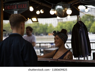 South Banks, London UK Sept 2018. 1950's Style Woman Behind The Counter Talking To A Customer, Smiling, Isolated