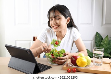 Mujer de la belleza del sudeste asiático que come la ensalada sana verde mientras que ve la película en la computadora de la tableta 