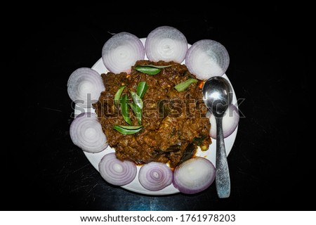 South Indian cuisine Kerala Style Beef fry / roast. Traditional style meat roast. Garnished with onion slices and curry leaves. Black background. Selective focus photograph.