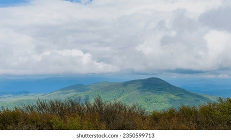 The south summit view from the peak of Elk Knob in North Carolina. Heavy white clouds hang over the Unicoi Mountain range in the foreground and the blue ridge mountain's layered peaks in the distance.
