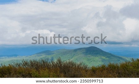 The south summit view from the peak of Elk Knob in North Carolina. Heavy white clouds hang over the Unicoi Mountain range in the foreground and the blue ridge mountain's layered peaks in the distance.