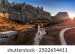 South Tyrol, Italy - Aerial panoramic view of the Chapel of San Maurizio (Cappella Di San Maurizio) at the Passo Gardena Pass in the Italian Dolomites at autumn with clear blue sky and setting sun