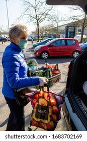 Southampton, England, UK. March 2020. An Elderly Woman Wearing A Face Mask And Rubber Gloves For Protection During The Coronavirus Epidemic Loading Her Grocery Shopping Into A Car.