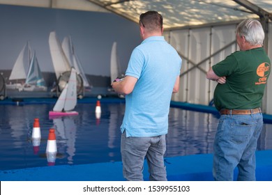 Southampton, Hampshire/UK - September 13 2019: Two middle aged men sail a remote control racing yacht on an indoor pool. One man watches as the other drives the boat. Mostly blue scene. 