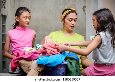 Southeast Asian Ethnicity Family Domestic Lifestyle. Stay At Home Mother Doing Laundry Helped And Accompanied By Her Children