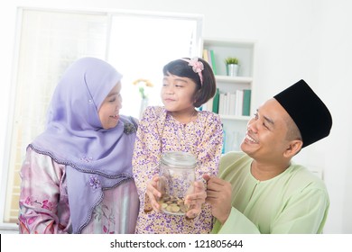 Southeast Asian Family. Muslim Girl Hand Holding Money Jar At Home.