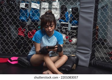 A Southeast Asian female boxer holding a cellphone, informs her parents through text messages that she is done with her training. - Shutterstock ID 2201083057