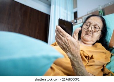 Southeast Asian female senior patient lying on hospital bed using smartphone for entertainment - Shutterstock ID 2196830091