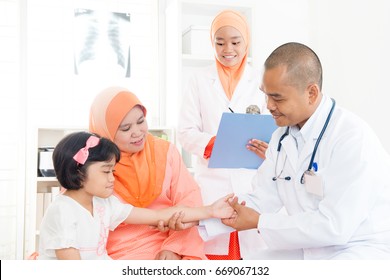 Southeast Asian Kid Patient Consulting Medical Doctor. Muslim Family. Little Girl With Broken Arm Doing Checkup.