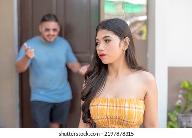 A Southeast Asian Lady Looks Sideways As She Listens To Her Angry Father Nagging Behind Her About Going Out Early In The Morning. Possible Domestic Violence.