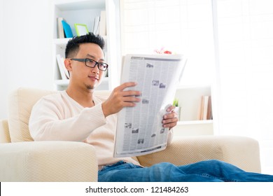 Southeast Asian Male Reading News Paper Sitting On Sofa At Home, Indoor Lifestyle