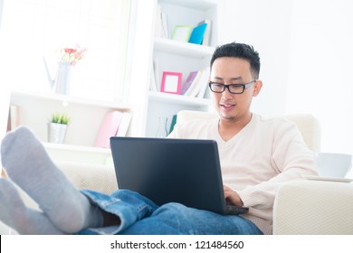 Southeast Asian Male Using Internet At Home, Sitting On Sofa Relaxing