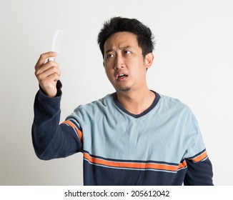 Southeast Asian Man Checking On A Comb With Shock Facial Expression, On Plain Background.