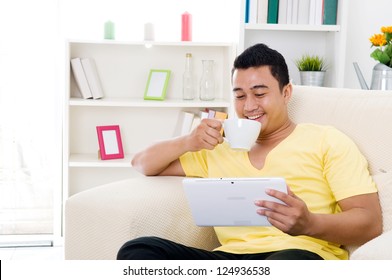 Southeast Asian Man Using Tablet Computer And Having Drinks At Home