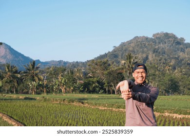 A Southeast Asian man wearing grey jacket with blue cap stretching arms for fitness, exercise and health, preparation and ready. Athlete, happy and warm up start outdoor for workout - Powered by Shutterstock