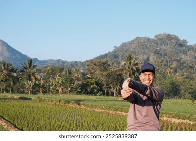 A Southeast Asian man wearing grey jacket with blue cap stretching arms for fitness, exercise and health, preparation and ready. Athlete, happy and warm up start outdoor for workout - Powered by Shutterstock