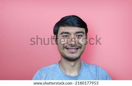 A southeast asian men smiling wearing a gray t-shirt on a pink background