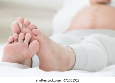 Southeast Asian Pregnant Women With Swelling Feet, Pain Foot And Lying On Bed In The Room. Swollen Feet And Fetal Poisoning Or Toxicity Concept