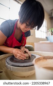 Southeast Asian Woman Sitting Down Centering Clay On A Potter Wheel In A Pottery Studio 