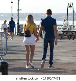 Southend-on-Sea Pier, Essex, England, 09-15-2019: Young Couple Walking Along The End Of Southend Pier Holding Hands