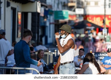 Southend-on-Sea, UK  August 8th 2022  A Black Man Wearing A Bucket Hat And Covid Mask Drinks Beer With His White Friend In A Pub Garden